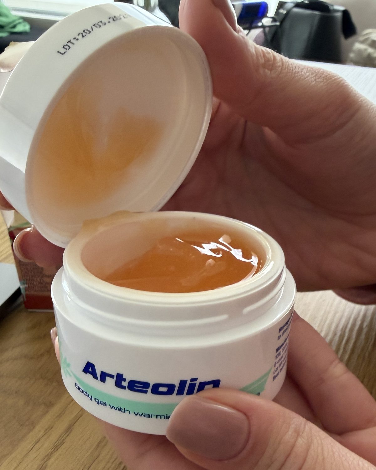 Kézben tartott nyitott Arteolin tégely fényes borostyánszínű géllel, felemelt kupakkal